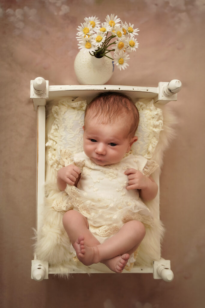 Neugeborenes im weißen Holzbettchen auf Spitzenkissen und Wolldecke